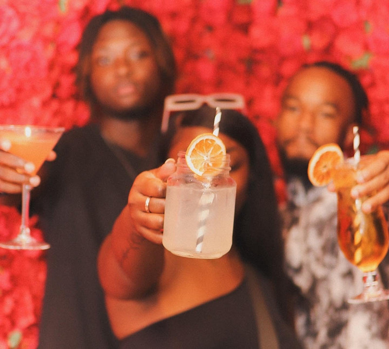 Three people holding drinks against a red floral background